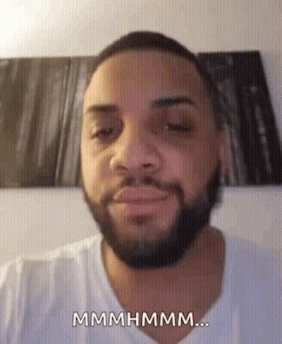 A Man With A Beard And A White Shirt Is Making A Funny Face And Saying Mmmmhmm . GIF