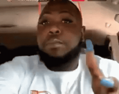 A Man With A Beard And A White Shirt Is Sitting In A Car Holding A Blue Object . GIF