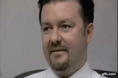 A Man With A Beard And A White Shirt Is Sitting In A Chair . GIF