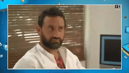 A Man With A Beard And A White Shirt Is Sitting In Front Of A Window With Blinds . GIF