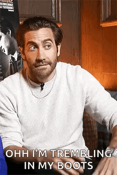 A Man With A Beard And A White Sweater Is Sitting On A Couch And Talking To Someone . GIF