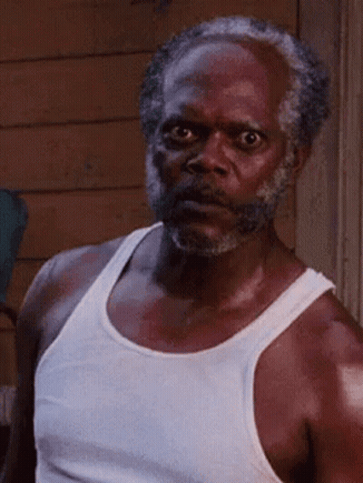 A Man With A Beard And A White Tank Top Is Looking At The Camera . GIF