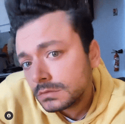 A Man With A Beard And A Yellow Hoodie Is Making A Face . GIF