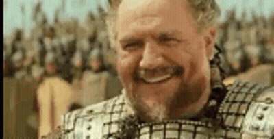 A Man With A Beard And Armor Is Smiling In Front Of A Crowd Of Soldiers . GIF