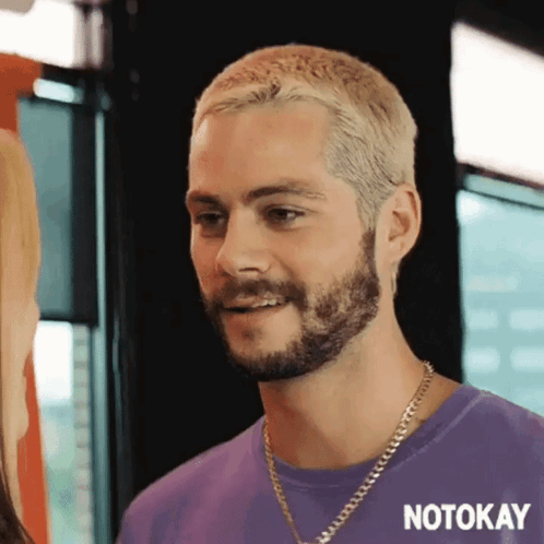 A Man With A Beard And Blonde Hair Is Wearing A Purple Shirt And A Chain . GIF