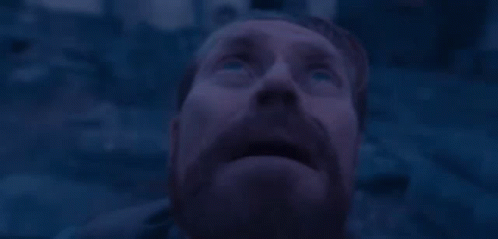 A Man With A Beard And Blue Eyes Is Looking Up At The Sky In The Dark . GIF