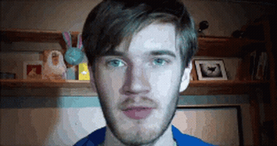 A Man With A Beard And Blue Eyes Is Standing In Front Of A Shelf With Pictures On It . GIF