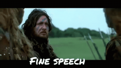 A Man With A Beard And Blue Paint On His Face Is Standing In A Field With Other People . GIF