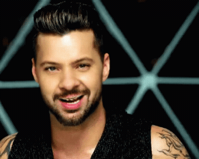 A Man With A Beard And Braces On His Teeth Is Smiling In Front Of A Geometric Pattern . GIF