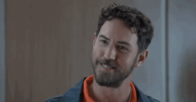 A Man With A Beard And Curly Hair Is Smiling While Wearing An Orange Shirt . GIF