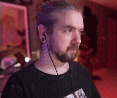 A Man With A Beard And Ear Plugs Is Wearing A Black Shirt . GIF