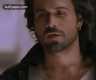 A Man With A Beard And Earrings Is Wearing A Leather Jacket . GIF