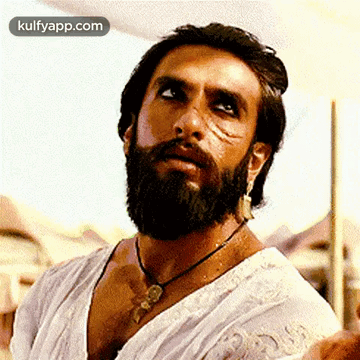 A Man With A Beard And Earrings Is Wearing A White Shirt And Necklace . GIF