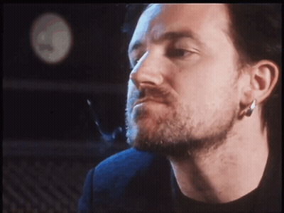 A Man With A Beard And Earrings Looks At The Camera GIF
