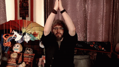 A Man With A Beard And Glasses Holds His Hands Together In Front Of A Stained Glass Lamp That Says Honey GIF