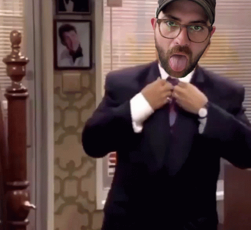 A Man With A Beard And Glasses Is Adjusting His Tie And Sticking His Tongue Out GIF