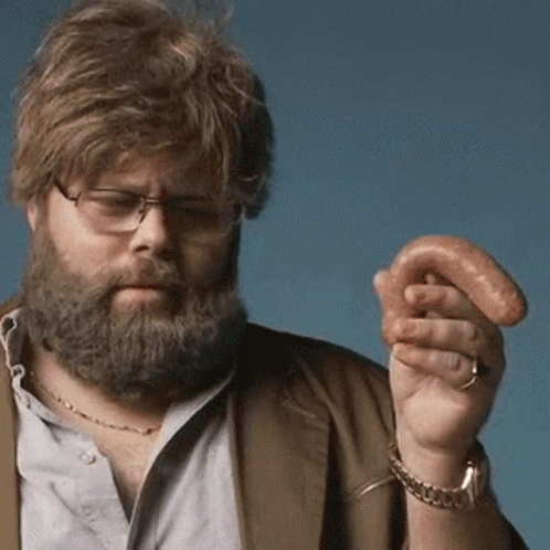 A Man With A Beard And Glasses Is Holding A Sausage In His Hand GIF