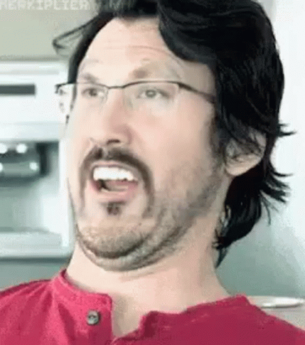 A Man With A Beard And Glasses Is Making A Funny Face In A Kitchen . GIF