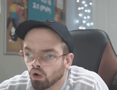A Man With A Beard And Glasses Is Sitting In A Chair Wearing A Hat And Glasses . GIF