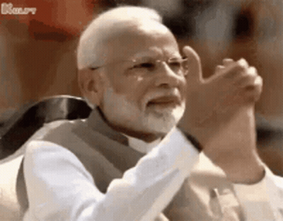 A Man With A Beard And Glasses Is Sitting In A Chair With His Hands In The Air . GIF
