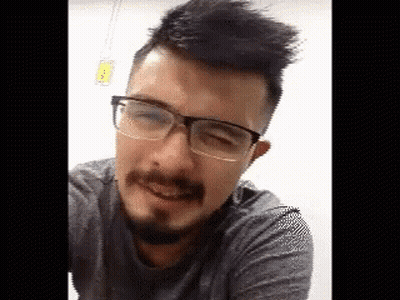 A Man With A Beard And Glasses Is Smiling And Looking At The Camera . GIF