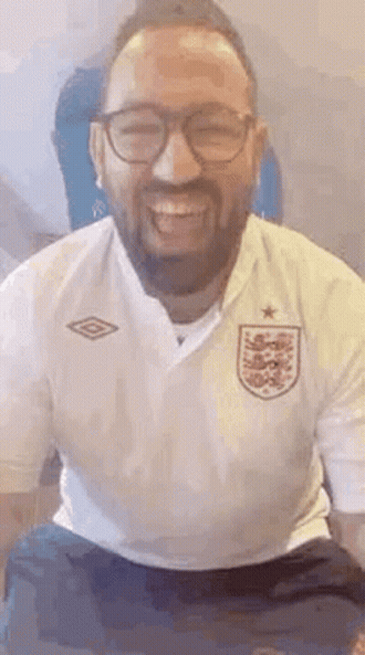 A Man With A Beard And Glasses Is Smiling And Wearing A White Shirt . GIF