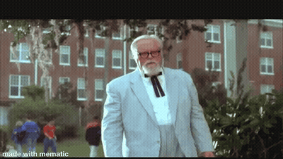 A Man With A Beard And Glasses Is Standing In Front Of A Brick Building . GIF