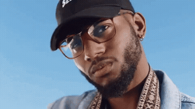 A Man With A Beard And Glasses Is Wearing A Baseball Cap And A Denim Jacket . GIF