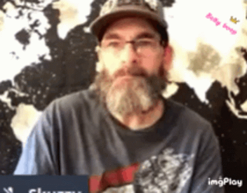 A Man With A Beard And Glasses Is Wearing A Hat And A Blue Shirt . GIF