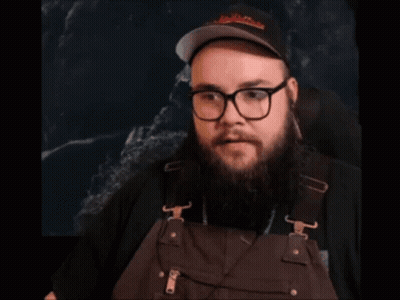 A Man With A Beard And Glasses Is Wearing Overalls And A Hat GIF