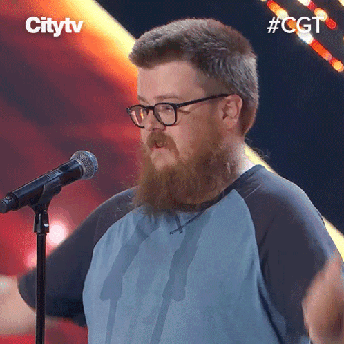 A Man With A Beard And Glasses Stands In Front Of A Microphone With The Hashtag #Cgt GIF