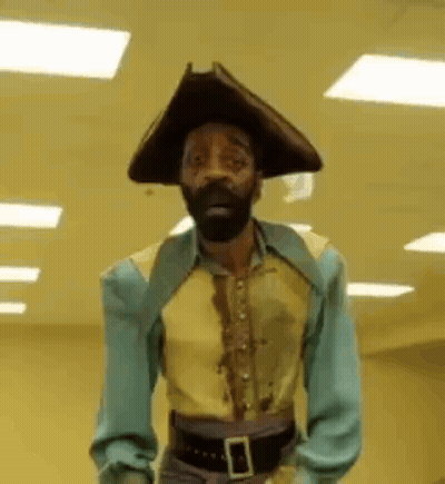A Man With A Beard And Hat Is Standing In A Hallway . GIF