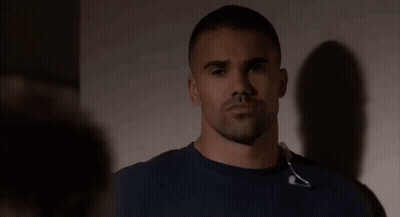 A Man With A Beard And Headphones Around His Neck Is Standing In Front Of A Wall . GIF