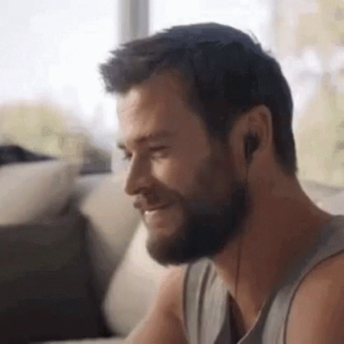 A Man With A Beard And Headphones Is Sitting On A Couch . GIF