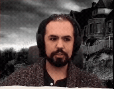 A Man With A Beard And Headphones Is Standing In Front Of A House . GIF