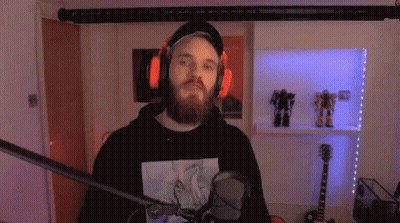 A Man With A Beard And Headphones Is Standing In Front Of A Microphone In A Room . GIF
