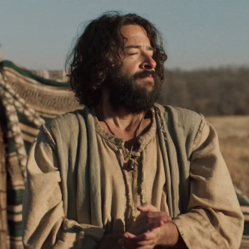 A Man With A Beard And Long Hair Is Standing In A Field GIF