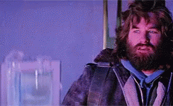 A Man With A Beard And Long Hair Is Standing In A Room With A Purple Background . GIF
