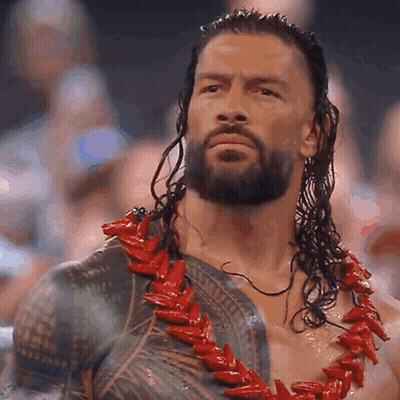 A Man With A Beard And Long Hair Is Wearing A Red Necklace . GIF