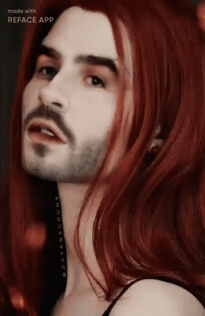 A Man With A Beard And Long Red Hair Is Looking At The Camera . GIF