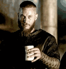 A Man With A Beard And Mustache Is Holding A Cup Of Coffee . GIF