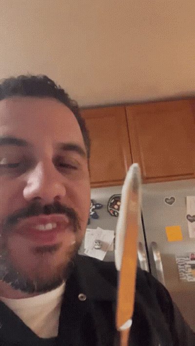 A Man With A Beard And Mustache Is Holding A Knife In Front Of A Refrigerator GIF