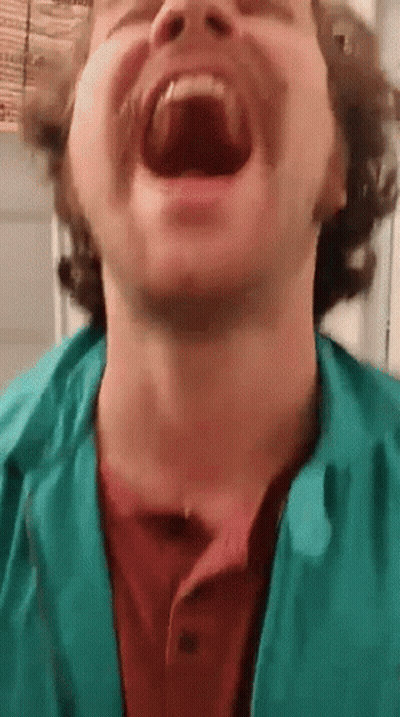 A Man With A Beard And Mustache Is Laughing With His Mouth Open . GIF
