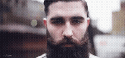 A Man With A Beard And Mustache Is Looking At The Camera With A Serious Look On His Face . GIF