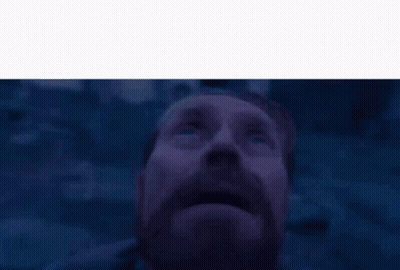 A Man With A Beard And Mustache Is Looking Up At The Sky In A Dark Room . GIF