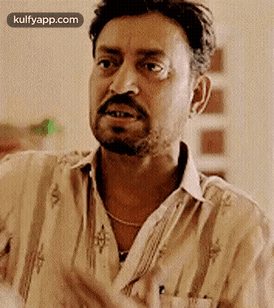 A Man With A Beard And Mustache Is Making A Funny Face While Wearing A Striped Shirt . GIF