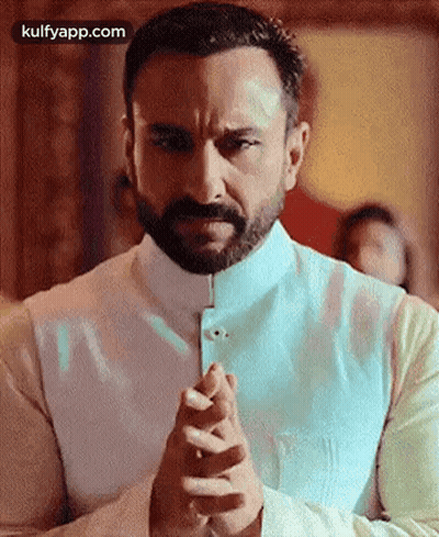 A Man With A Beard And Mustache Is Praying With His Hands Folded . GIF