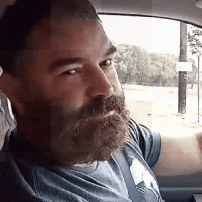A Man With A Beard And Mustache Is Sitting In A Car . GIF