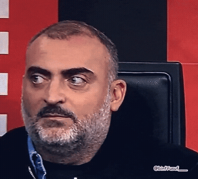 A Man With A Beard And Mustache Is Sitting In A Chair With Bin / Yusuf Written On The Bottom Right GIF