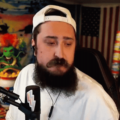 A Man With A Beard And Mustache Is Sitting In Front Of A Microphone Wearing Headphones And A White Hat . GIF